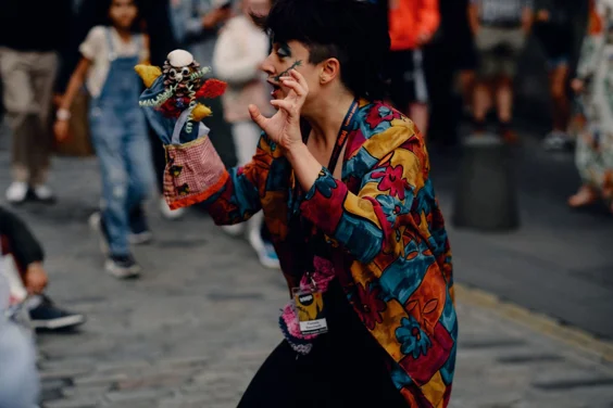 photo shows close up of female puppeteer in bright shirt performing on Edinburgh's royal mile with patchwork puppet