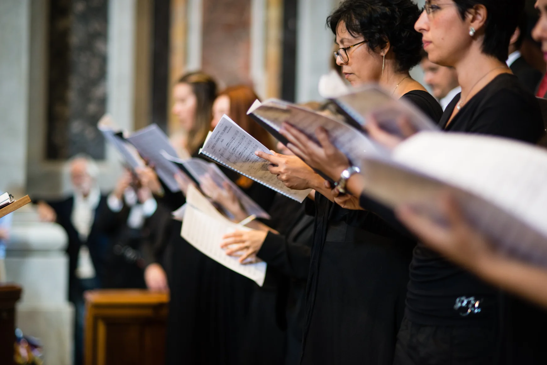 A group of females singers wearing black clothes hold booklets of sheet music. 