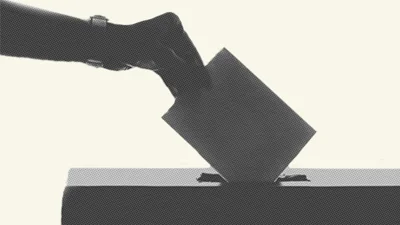 Grey-coloured close up of a person's hand and arm placing a ballot card into a general election ballot box.